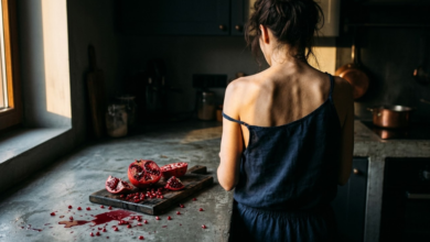 Moteris stovi prie pilko virtuvės stalviršio, ant kurio guli netvarkingai perpjautas ryškiai raudonas granatas
