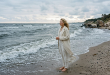 moteris šviesiais drabužiais stovi prie banguojančios, pilkšvos Baltijos jūros ankstų rytą