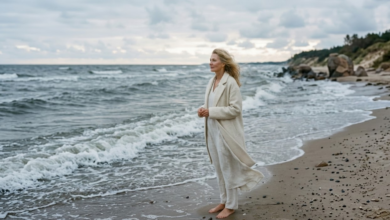 moteris šviesiais drabužiais stovi prie banguojančios, pilkšvos Baltijos jūros ankstų rytą