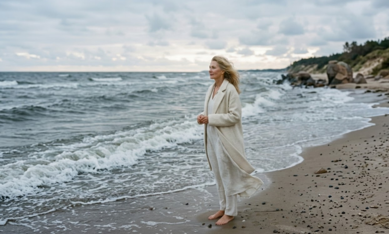 moteris šviesiais drabužiais stovi prie banguojančios, pilkšvos Baltijos jūros ankstų rytą