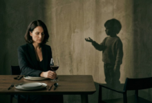 moteris sėdi prie stalo su vyno taure, o ant sienos vaiko šešėlis, tiesiantis ranką