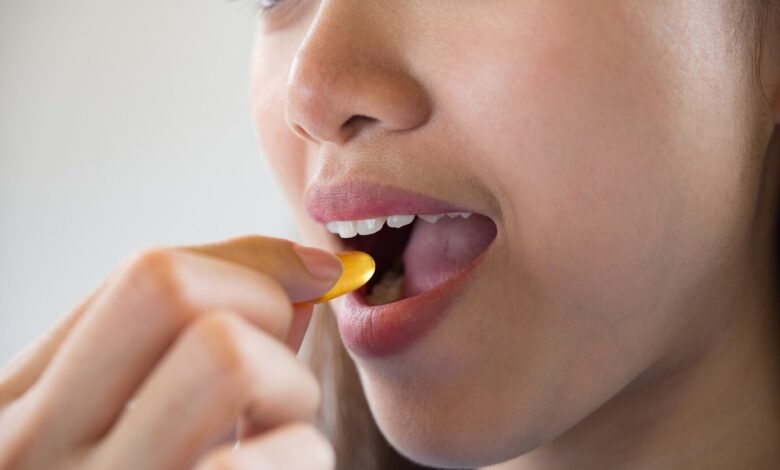 Moteris deda į burną vitamino kapsulę