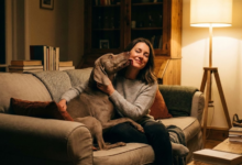 Moteris sėdi ant sofos, o jos šuo švelniai laižo skruostą