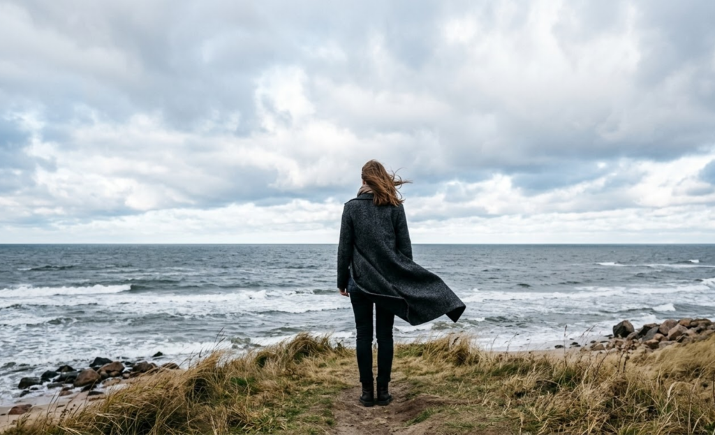 Moteris iš nugaros stovi priešais beribę, pilką jūrą