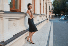 jauna mergina apsirengusi sijoną pieštuką stovi prie namo sienos