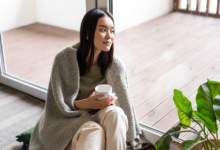 japonė moteris sėdi namie su puodeliu rankoje prie lango