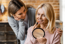 vyresnė moteris dažosi lūpas prieš veidrodį, jaunesnė žiūri