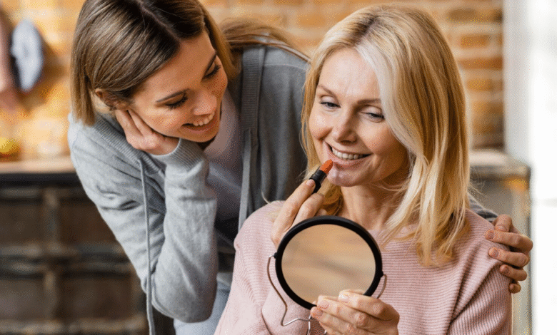 vyresnė moteris dažosi lūpas prieš veidrodį, jaunesnė žiūri