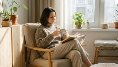 40 metų moteris sėdi fotelyje namie su knyga ir arbatos puodeliu