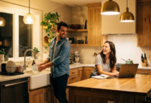 moteris dirba virtuvėje kompiuteriu, vyras plauna indus