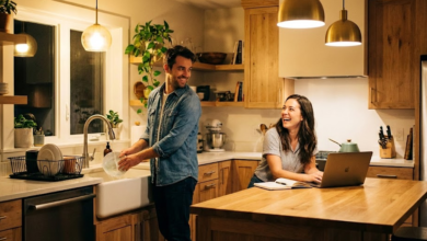 moteris dirba virtuvėje kompiuteriu, vyras plauna indus