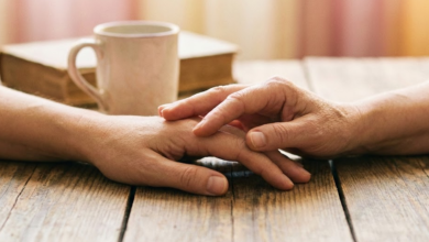 Dvi rankos, švelniai liečiančios viena kitą ant stalo paviršiaus