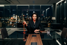 griežto stiliaus juodą kostiumą dėvinti moteris, sėdinti derybų stalo gale