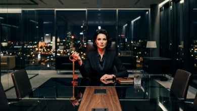 griežto stiliaus juodą kostiumą dėvinti moteris, sėdinti derybų stalo gale