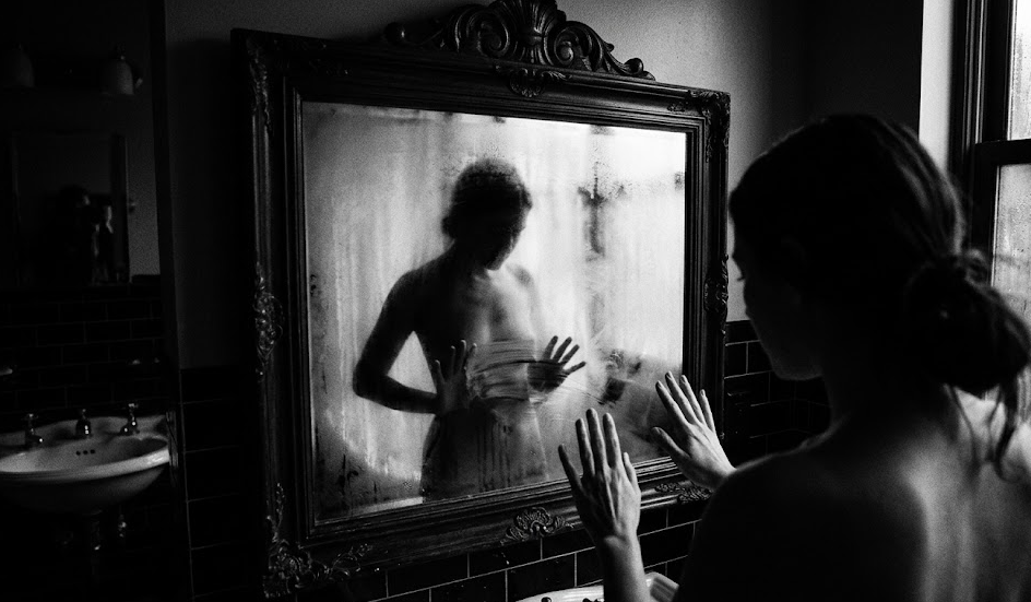 moteris stovi nuoga prieš rasotą veidrodį. nuotrauka juodai balta